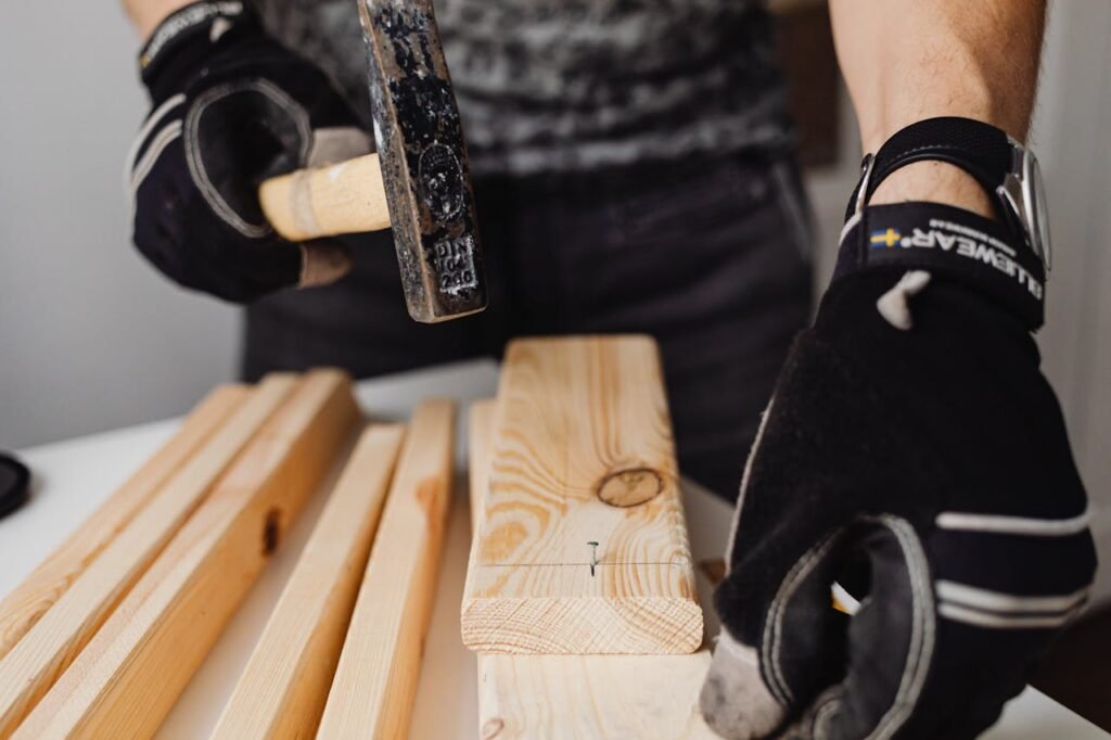 Transform Your Home with Mr. M Handyman: Essential Services You Can Trust A carpenter wearing gloves uses a hammer to drive nails into wooden planks in a workshop.